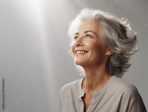 Beautiful gray-haired senior woman with happy smile looking up on a light grey background photo