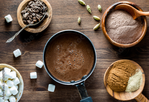 A look into a small pot of hot cocoa with ingredients all around to make it. © Carey