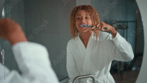 cheerful woman dressed white bathrobe standing in front of mirror holding toothbrush brushing the teeth with braces oral and gum care for healthy photo