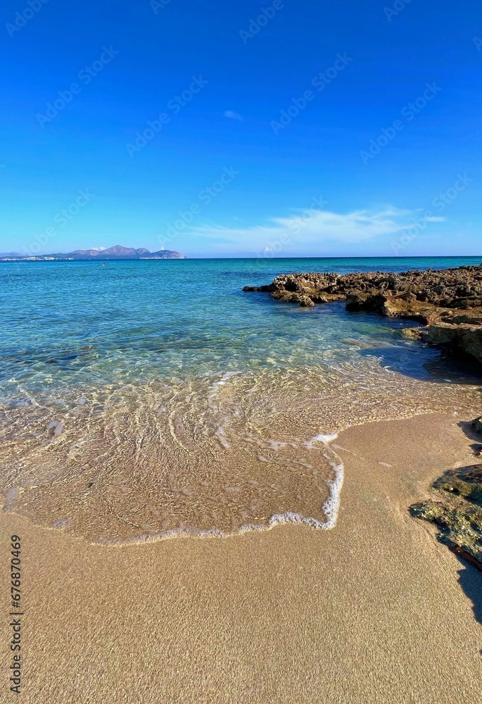Vertical shot of sea waves on a sandy beach under a blue sky. Vertical shot of sea waves on a sandy beach under a blue sky.