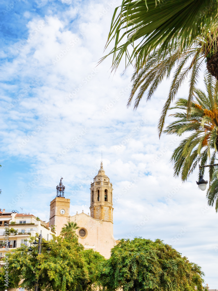 Church of St. Bartholomew and Santa Tecla in Sitges, Catalonia, Spain against a background of blue sky, palm trees and plants, vertical photo with copy space