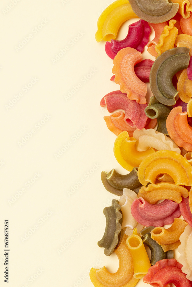 Food background with row of shaped three colored  pasta with spinach beetroot and tomato additive on yellow background with copy space