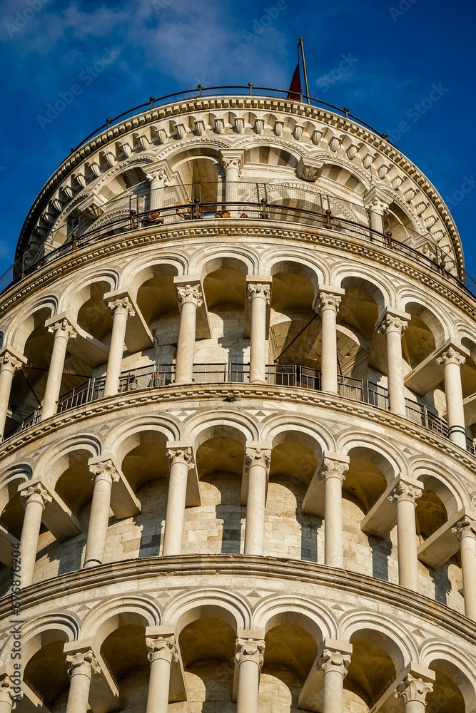 Vertical shot of the top half of a large leaning tower of Pisa under blue sky