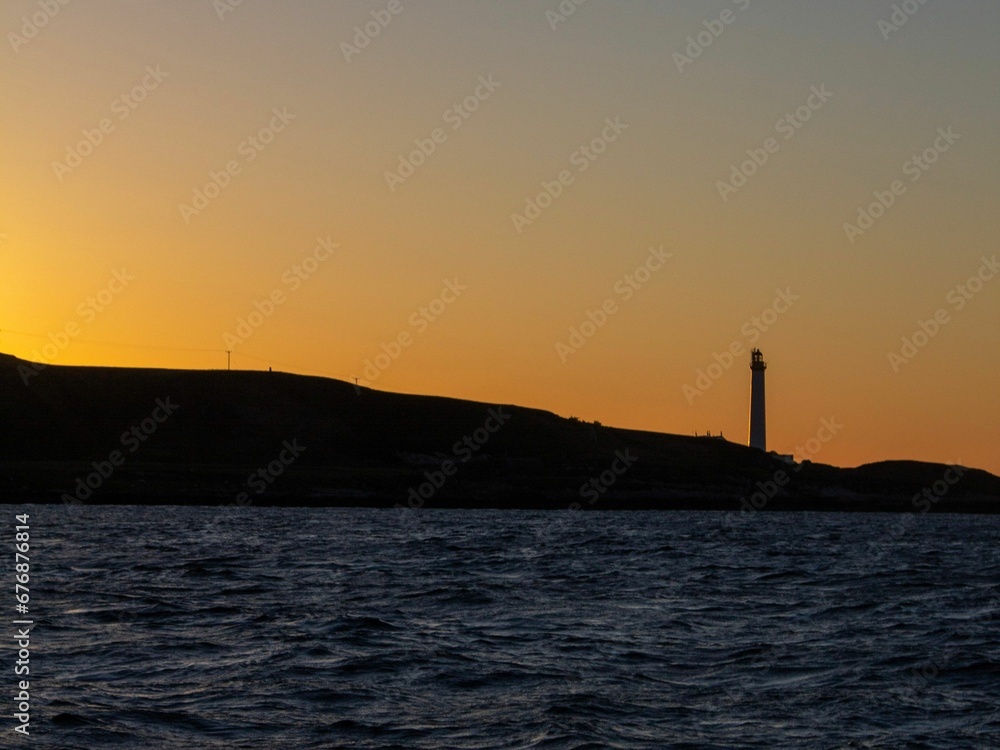 Breathtaking view of orange sunset sky and lighthouse silhouette above the sea - beautiful wallpaper
