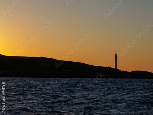 Breathtaking view of orange sunset sky and lighthouse silhouette above the sea - beautiful wallpaper