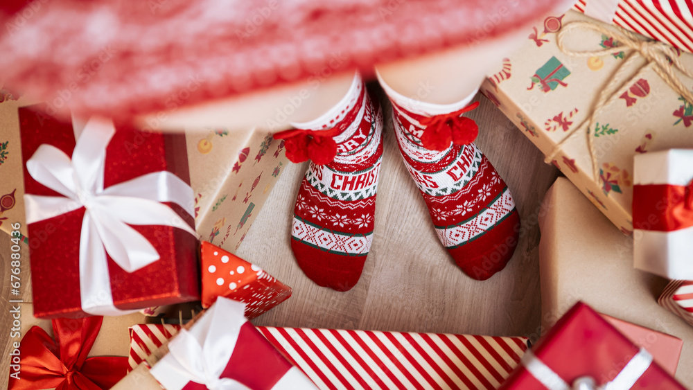 Fototapeta premium A woman, cozy and warm in a cute red socks, poses by Christmas tree, box gifts