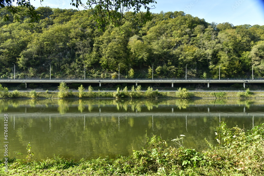 Reflet dans les eaux de la Meuse de la colline boisée et de l'autoroute à Lustin Reflet dans les eaux de la Meuse de la colline boisée et de l'autoroute à Lustin