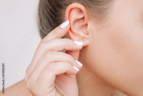 Ear piercing. Cropped shot of a young woman wearing elegant stud earrings on a gray background. Jewelry with gemstones, accessories photo