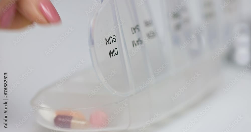 Woman hand putting pills into open pill organizer or plastic pillbox Woman hand putting pills into open pill organizer or plastic pillbox
