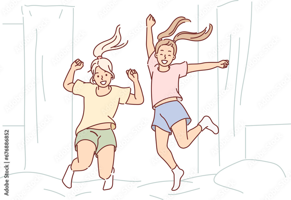 Cheerful girls are jumping on bed in bedroom, not wanting to go to sleep due to hyperactivity