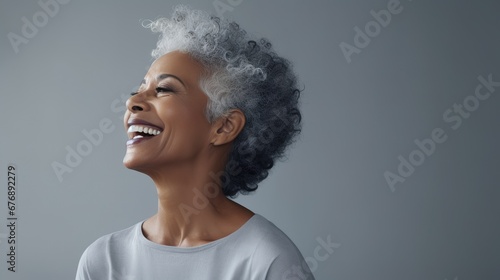 A black elderly woman with gray afro hair smiles and poses against a light gray studio background. skin care for 50-60 years
