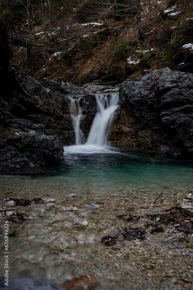 Vertical of a beautiful natural scenery of foamy water falling down the rocks into a turquoise pool Vertical of a beautiful natural scenery of foamy water falling down the rocks into a turquoise pool