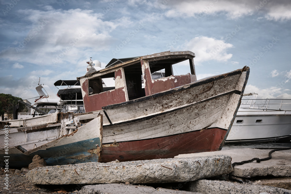 An old broken wooden fishing boat against the background of modern yachts.