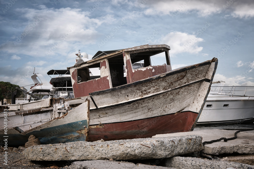 An old broken wooden fishing boat against the background of modern yachts. An old broken wooden fishing boat against the background of modern yachts.