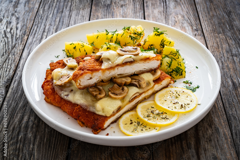 Crispy breaded seared chicken cutlet with fried white mushrooms, cheese and boiled potatoes on wooden table
Crispy breaded seared chicken cutlet with fried white mushrooms, cheese and boiled potatoes on wooden table