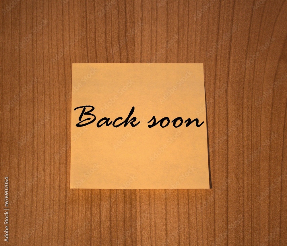 Post-it note Back soon wooden background Post-it note Back soon wooden background