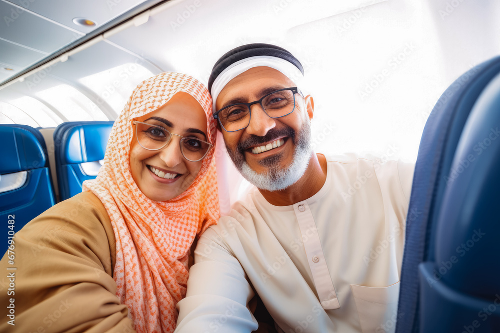 Happy smiling older arab tourist couple taking selfie inside airplane. Tourism concept, holidays and traveling lifestyle.