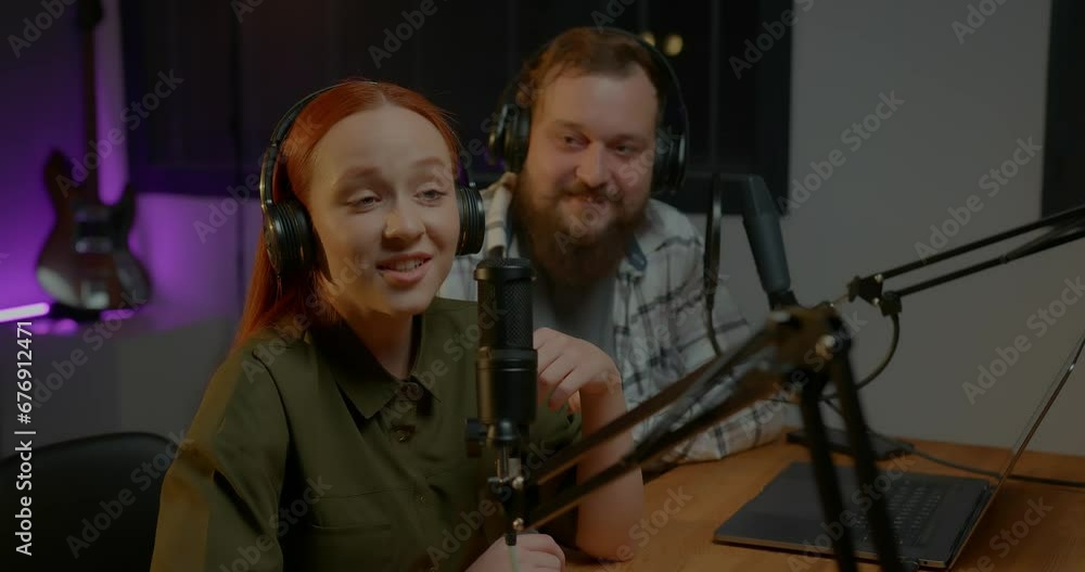 two radio hosts in headphones laughing while recording podcast in studio together
two radio hosts in headphones laughing while recording podcast in studio together