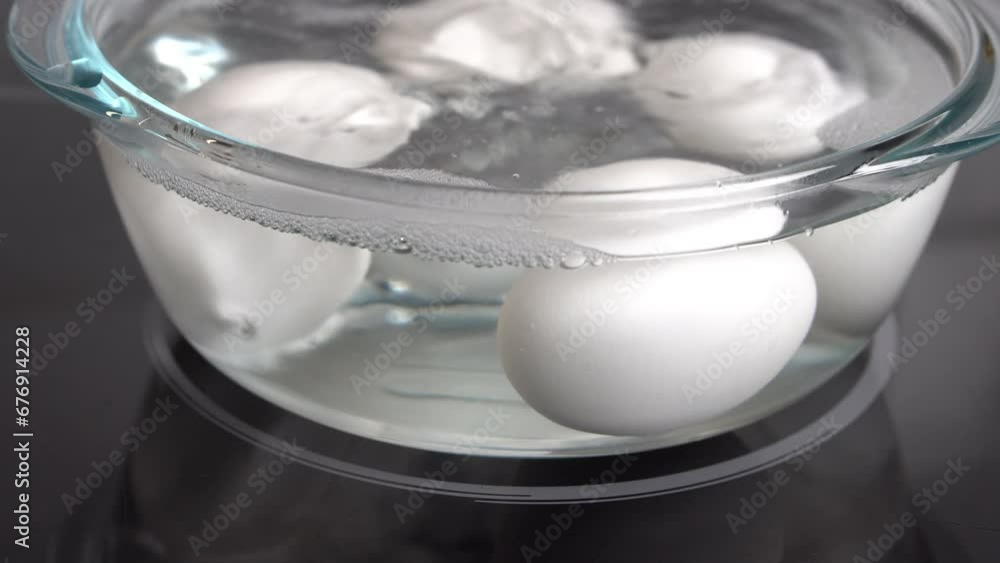 Slow motion shot of white eggs boiling in a transparent glass pot on an electric stove. Slow motion shot of white eggs boiling in a transparent glass pot on an electric stove.