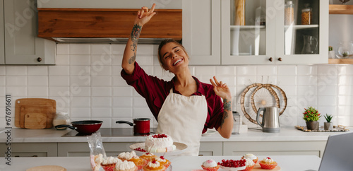 Fotografi Joyful female baker in apron dancing while making cakes and muffins at the domes
