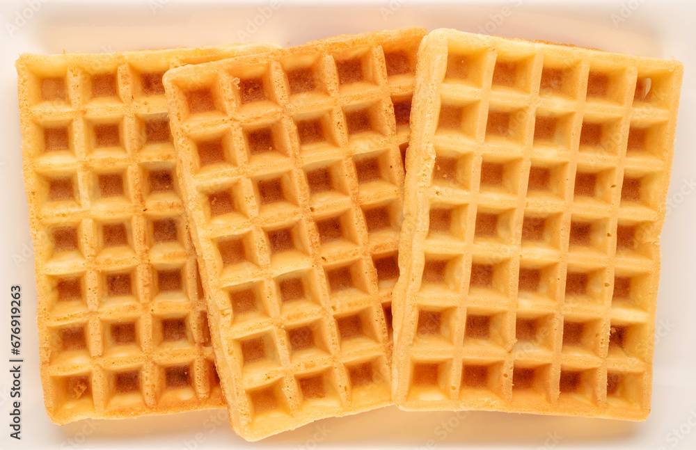 Three freshly baked aromatic waffles on a ceramic white plate, macro, top view. Three freshly baked aromatic waffles on a ceramic white plate, macro, top view.