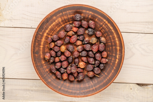 Several dry rosehip berries with ceramic plate on wooden table, macro, top view.