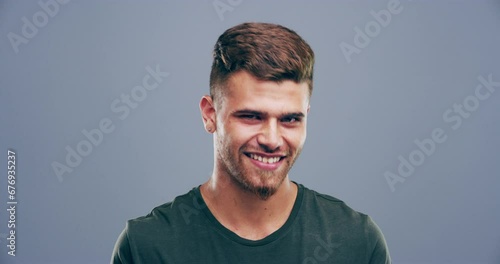 Confident, wink and face of man on gray background for happiness, flirting and romance gesture in studio. Smile, body language and portrait of happy person with reaction for secret, comic and emoji photo