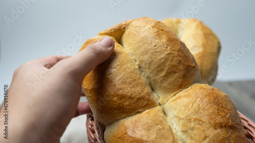 Man's hand taking a traditional Chilean Marraqueta bread, in a bread basket with white background on gray wooden table.