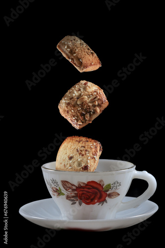 Freshly baked chocolate chips cookies and white designer tea cup or coffee cup isolated on black background.