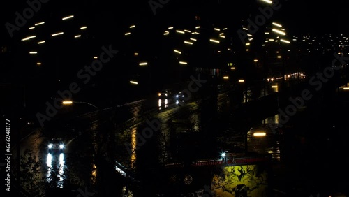 Cars drive along the night road in the rain. Cars headlights and night city lights are reflected on the wet road. Beautiful view of cars and vehicles driving on the highway. 4k Video footage for news