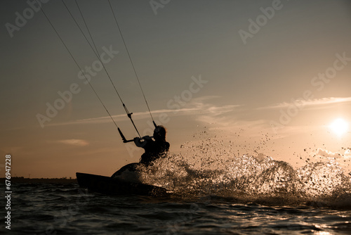 Female wakeboarder rides a wakeboard, holding on to a handle on a cable against the background of the sunset