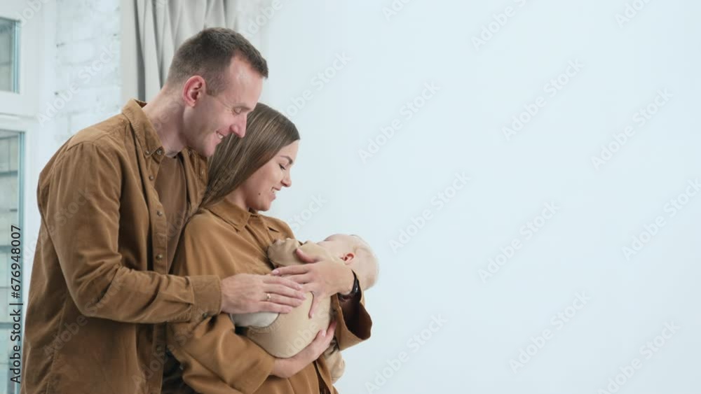 Charming Caucasian parents looking at their sleeping child with love. Happy parents with infant stand at the window. Charming Caucasian parents looking at their sleeping child with love. Happy parents with infant stand at the window.