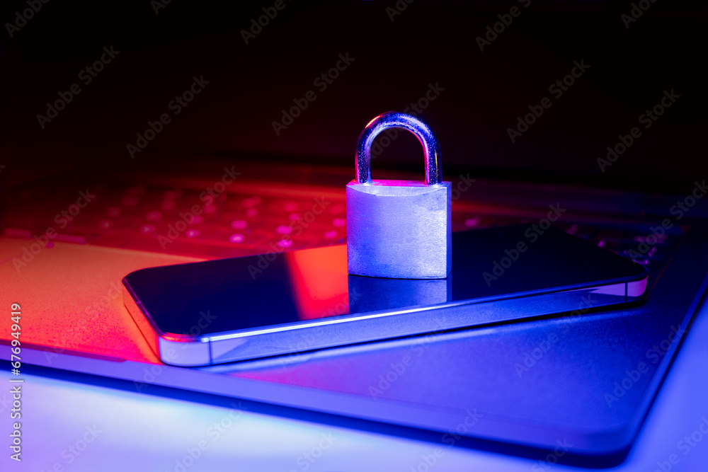 Closeup of a padlock on a laptop and phone illuminated with blue and red light.Phishing, cybersecurity danger or ransomware attack. Encrypted privacy in email. Closeup of a padlock on a laptop and phone illuminated with blue and red light.Phishing, cybersecurity danger or ransomware attack. Encrypted privacy in email.