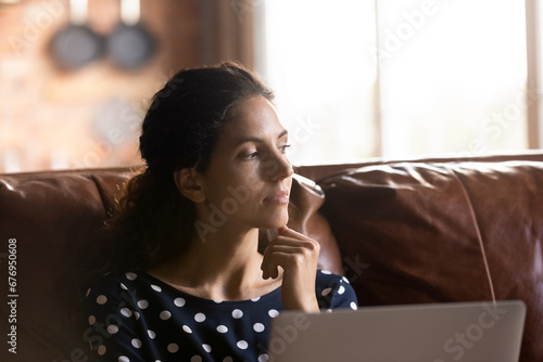 Close up thoughtful woman distracted from laptop, sitting on couch, looking to aside and touching chin, pensive young female feeling unmotivated, freelancer working on online project at home