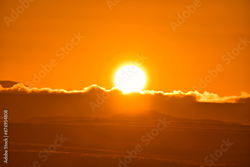 Sonnenaufgang in der Wüste hinter einer Düne über Wolken am Himmel