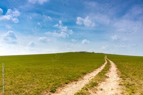 Beautiful shot of a dirt road between green fields under a cloudy sky