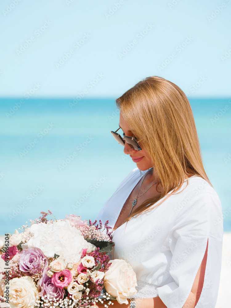 Joyful Young Woman Holding a Bouquet of Flowers on a Beach with Blue Sky Background