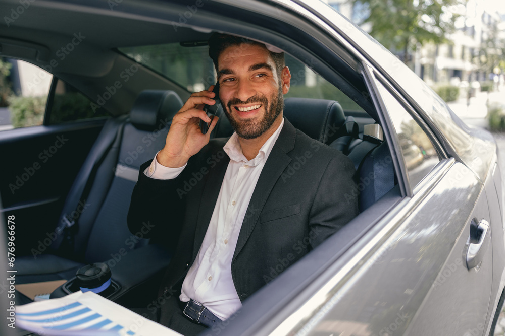 Smiling businessman talking phone with client while sitting on car backseats. High quality photo