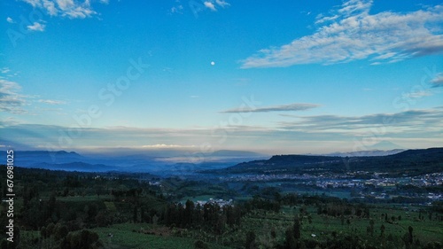 Fototapeta Naklejka Na Ścianę i Meble -  Beautiful blue sky above a green valley with trees and a rural community