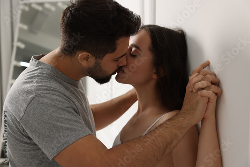 Passionate young couple kissing near white wall indoors
