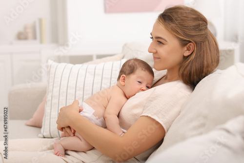 Mother holding her cute newborn baby on sofa at home, space for text