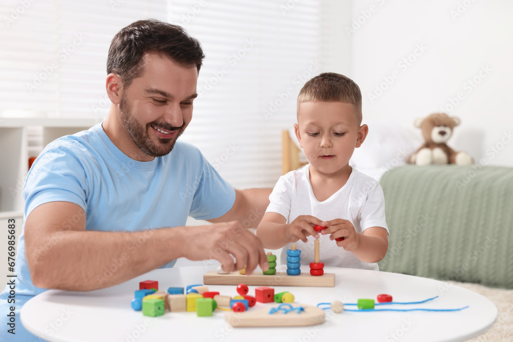 Motor skills development. Father and his son playing with stacking and counting game at table indoors Motor skills development. Father and his son playing with stacking and counting game at table indoors