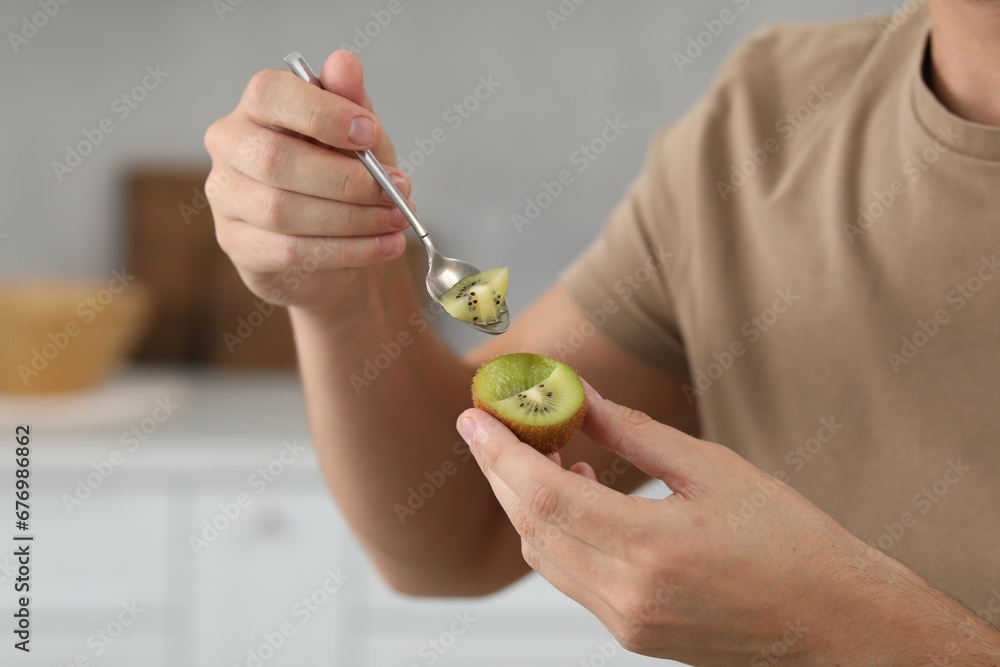 Man eating kiwi with spoon on blurred background, closeup