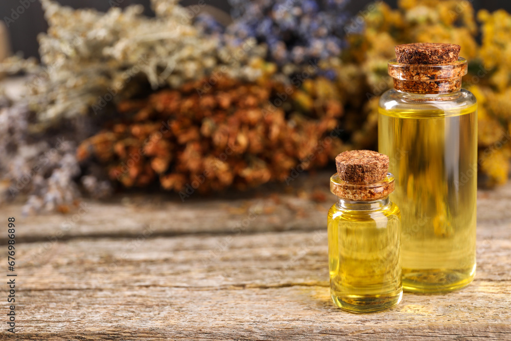 Bottles of essential oils and many different dry herbs on wooden table, closeup. Space for text Bottles of essential oils and many different dry herbs on wooden table, closeup. Space for text