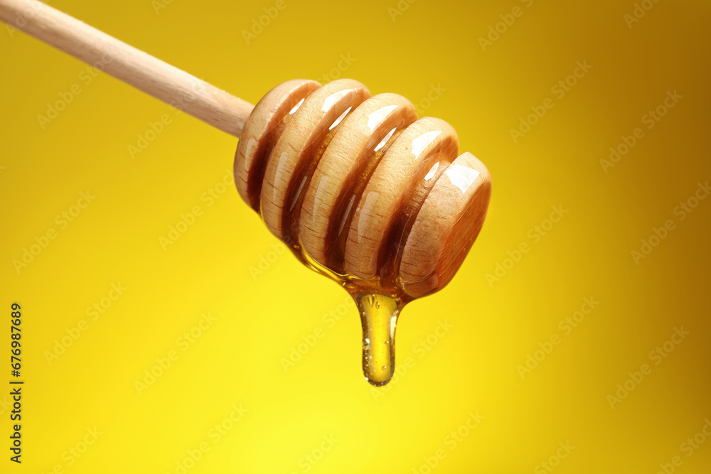 Delicious honey flowing down from dipper against yellow background, closeup Delicious honey flowing down from dipper against yellow background, closeup