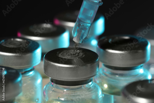 Filling syringe with medicine from vial against dark background, closeup