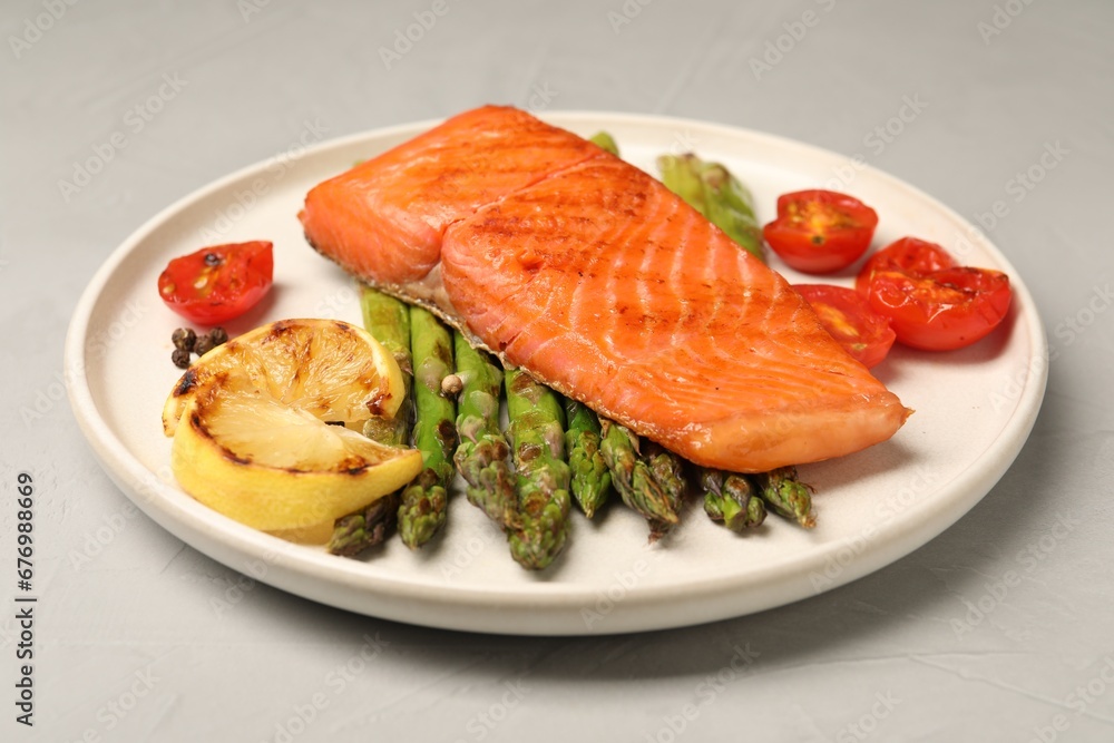 Tasty grilled salmon with asparagus, tomatoes, spices and lemon on light grey table Tasty grilled salmon with asparagus, tomatoes, spices and lemon on light grey table