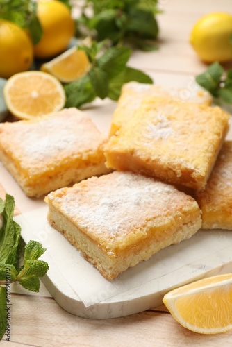 Tasty lemon bars with powdered sugar and mint on wooden table  closeup