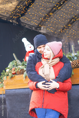 Happy girl and boy hugging in front of Christmas decoration in winter.