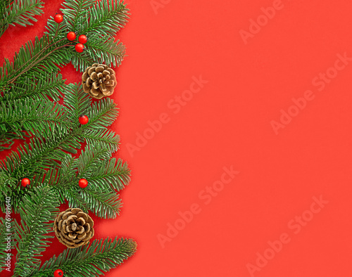 Green fir branches with red berries and brown cones on the left on the red background.